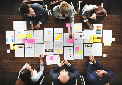 Ein Unternehmenskauf sollte im Vorfeld sorgfältig geplant werden Planungsmeeting mit sechs Teilnehmern, die Unterlagen diskutieren.