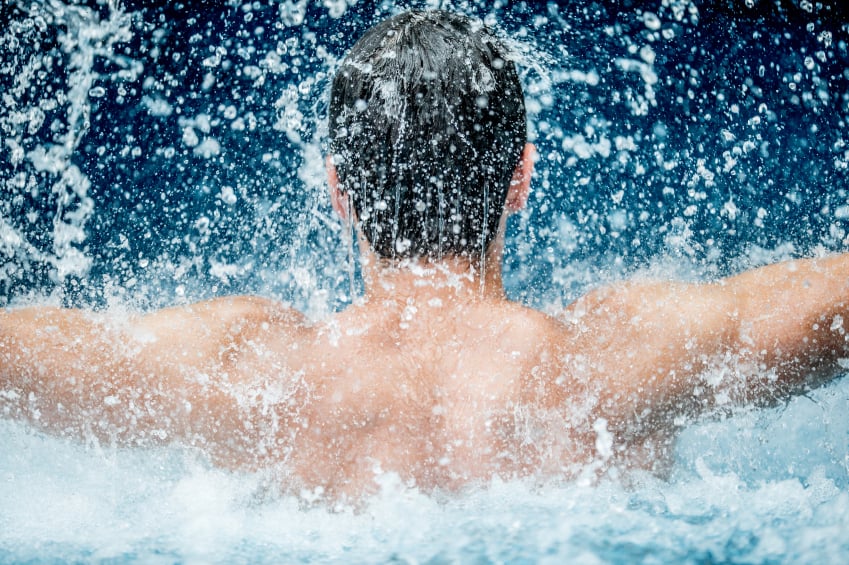 Schwimmbad Mann springt mit ausgebreiteten Armen aus dem Wasser